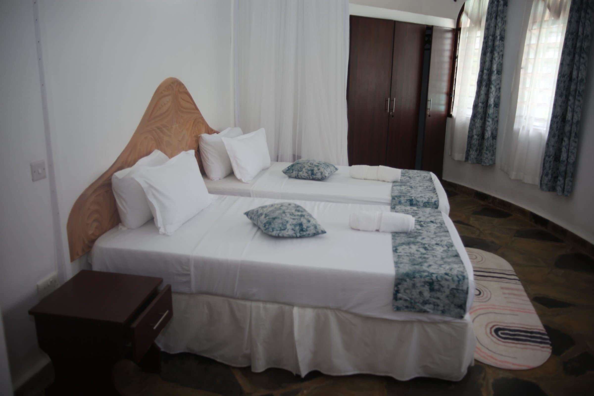 Bedroom inside a Two-Bedroom Family Cottage configured with twin beds, a carved Swahili-style headboard and white linens with coastal-blue accents